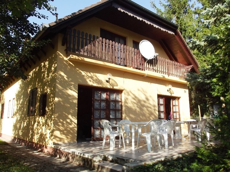 Egy sárga színű, kétszintes nyaraló, terasszal és műholdas antennával.